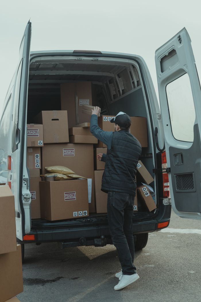 A courier organizing boxes in a delivery van for shipment on a cloudy day.
